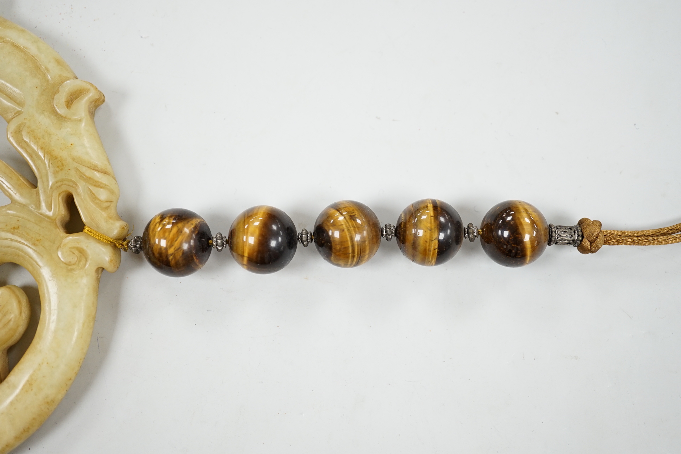 A large Chinese bowenite jade disc, threaded with tiger's eye beads and long silk tassel, 90cm long